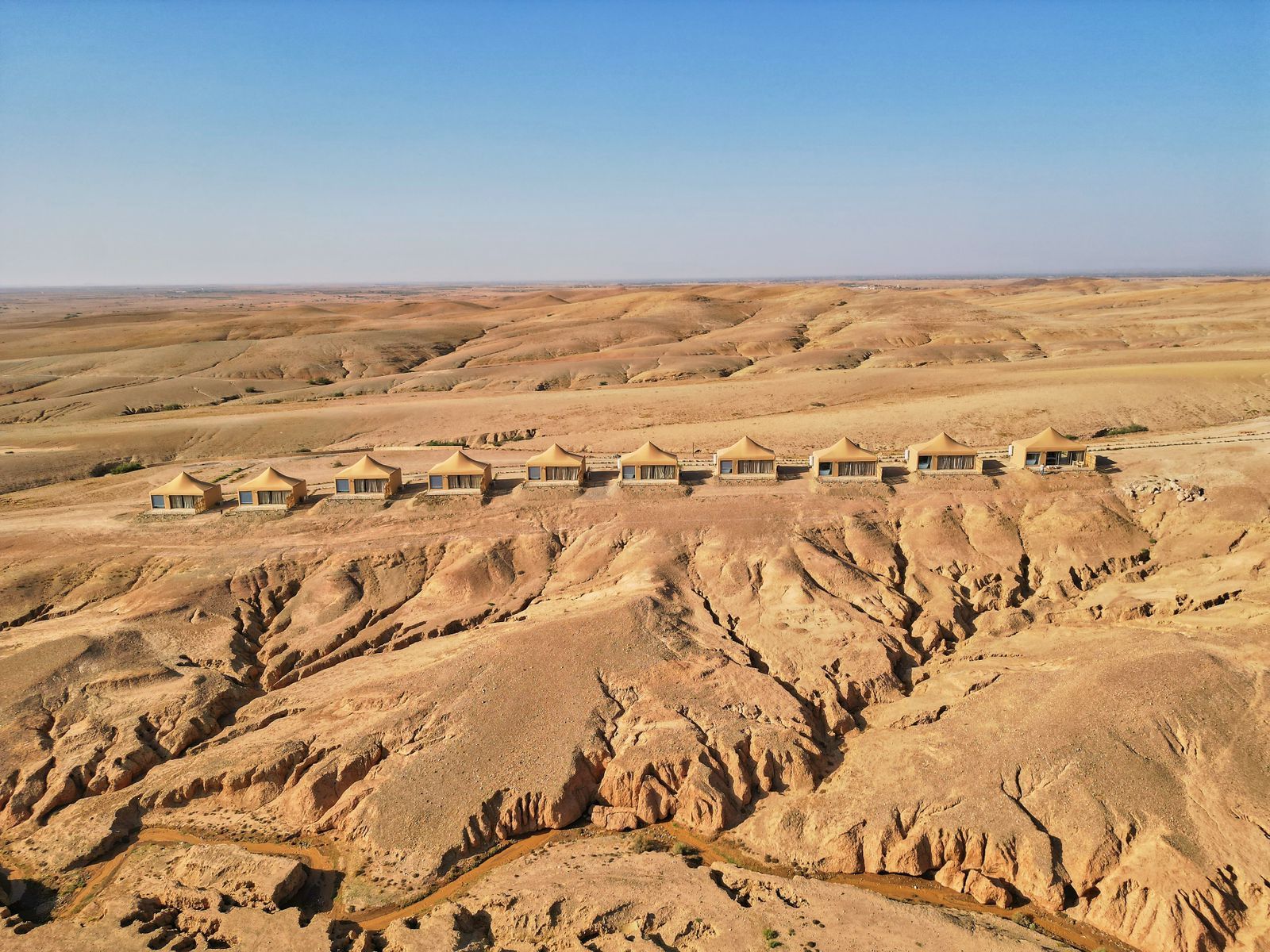 Aerial view of a line of luxury tents along a ridge in the stone desert of Agafay