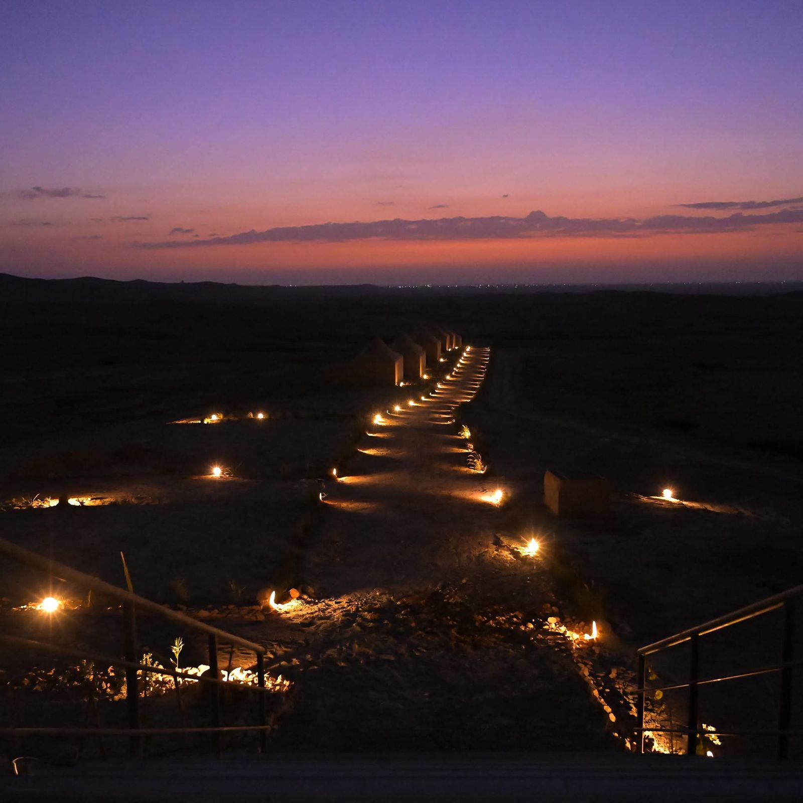 Lantern-lit path leading to a line of tents on the Agafay plateau at dusk