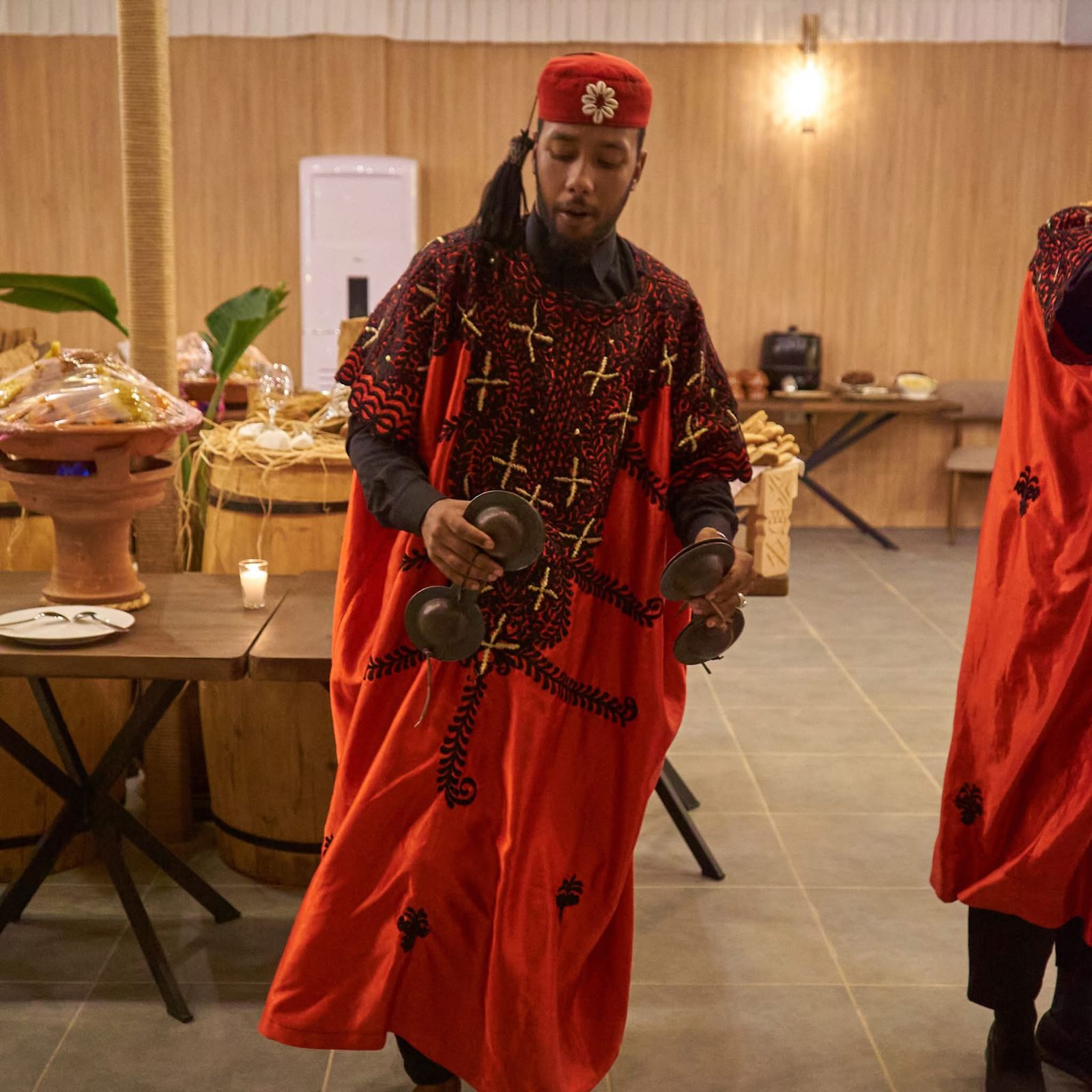 Gnawa musicians in embroidered red robes playing qraqeb during dinner service at the camp