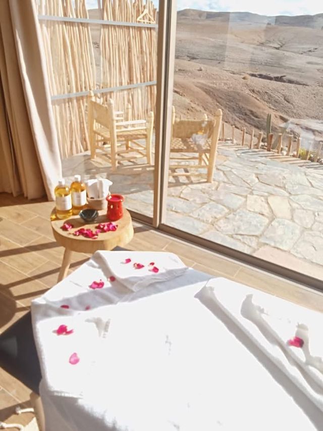 Lettino da massaggio con petali di rosa e oli, davanti a una finestra sulle colline del deserto