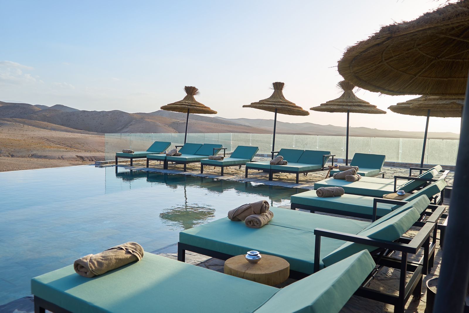 Infinity pool and parasols overlooking the stone hills of the Agafay Desert in daylight