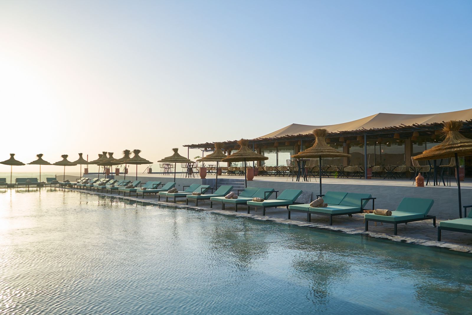Liegen und Sonnenschirme am Pool eines Agafay-Camps im Morgenlicht