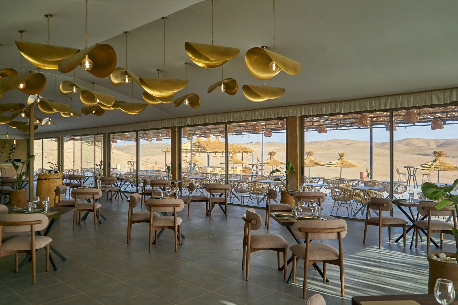 Restaurant under canvas with brass pendant lights and glass walls onto the desert