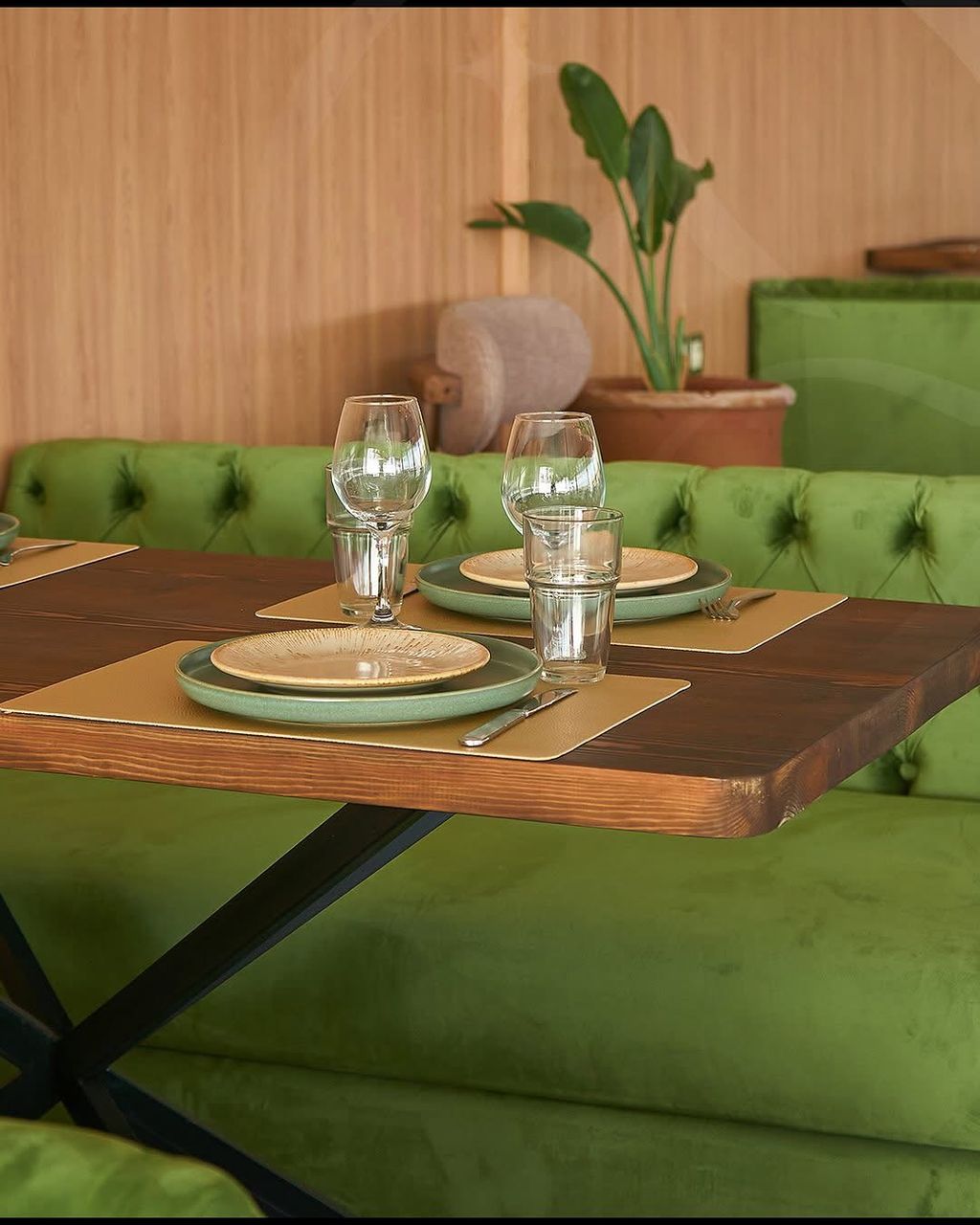 Table laid with green ceramic plates and glassware against a velvet banquette in the restaurant