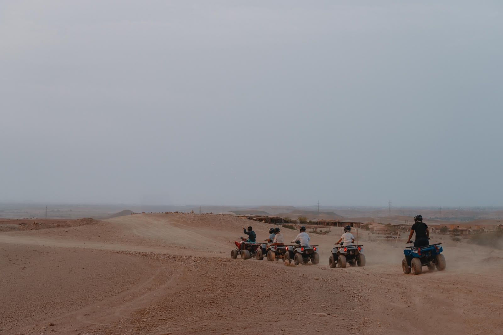 Quadrijders verspreid over open zand op het Agafay-plateau in heiig licht