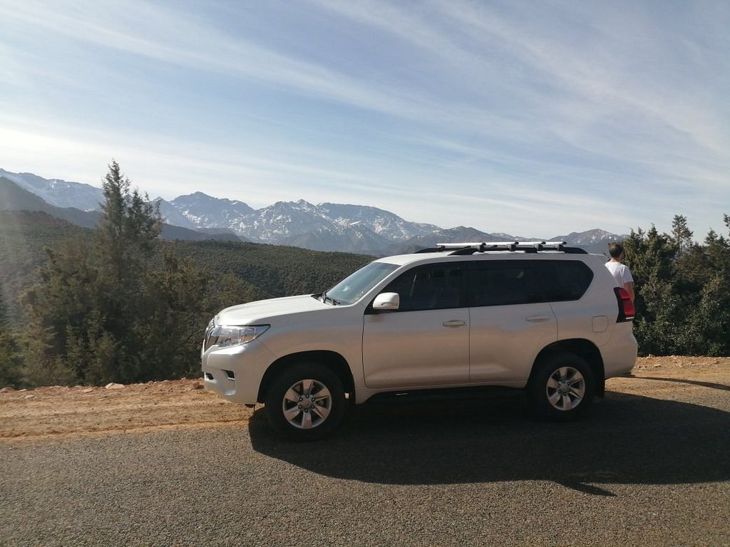 Toyota Land Cruiser Prado bianco fermo su una strada di montagna, l’Alto Atlante innevato dietro