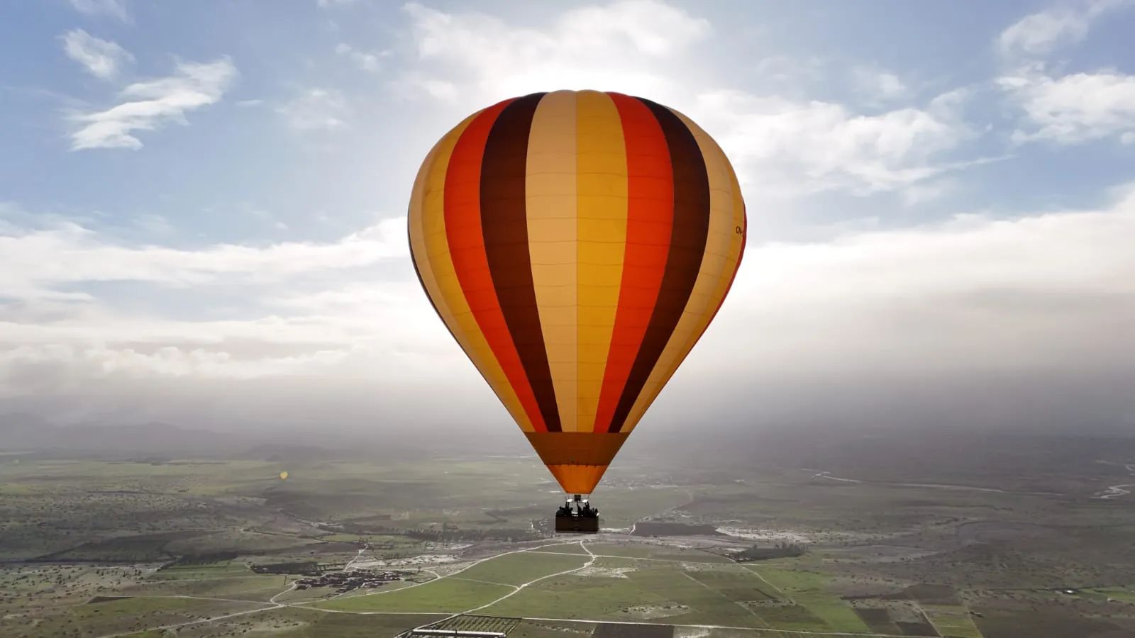 A single hot air balloon drifting over the plain outside Marrakech under a wide morning sky