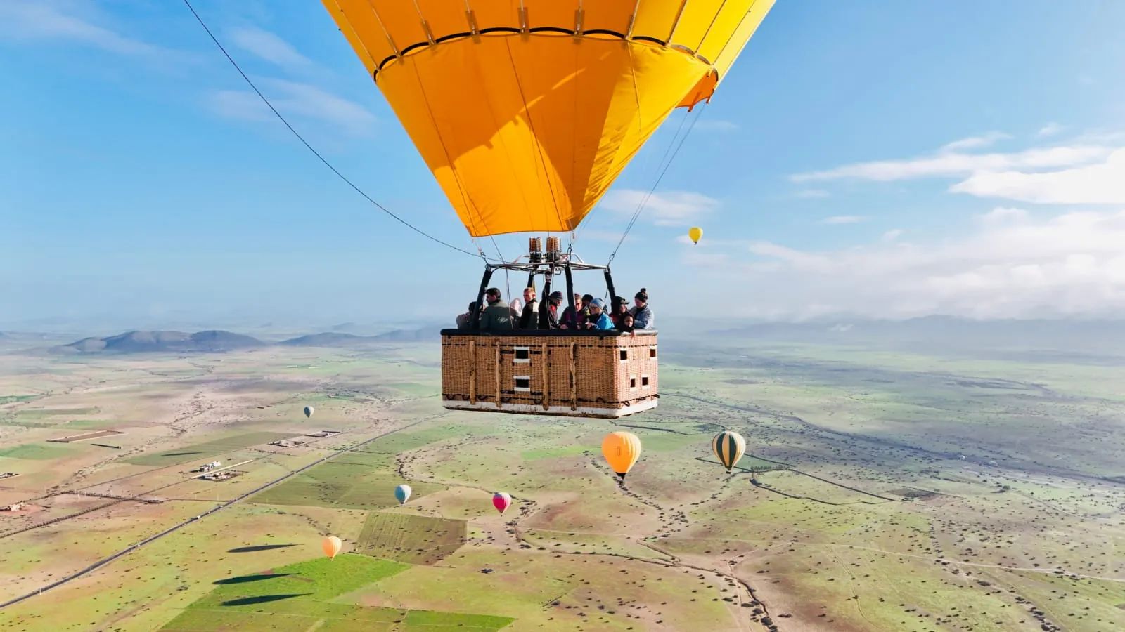 Passengers in a wicker balloon basket above the fields near Marrakech, other balloons around them